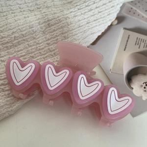 Dettaglio della molletta per capelli in acetato rosa con motivi a cuore e resina