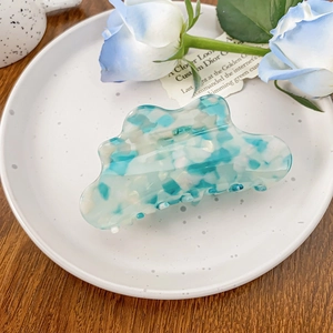 Dettaglio di un fermaglio per capelli in acetato con motivo marmorizzato blu e bianco