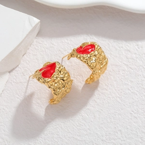 Irregular hammered gold earrings with red heart enamel inlay on white artistic background