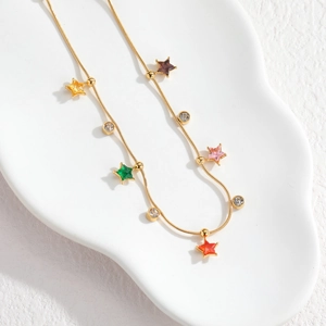 Golden necklace with colorful star pendants and clear zircons on a white tray