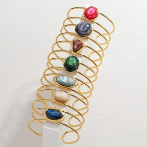 Detail view of seven golden open cuffs featuring colorful marble and mother-of-pearl stones