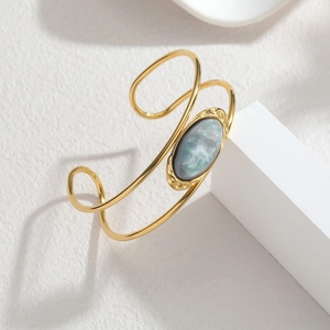 Macro detail of gold-plated open bangle featuring a blue stone on white pedestal