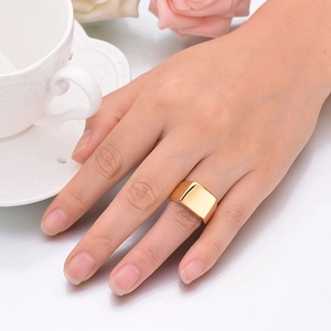 Close-up of polished gold-plated square signet ring worn on a finger with lifestyle decor