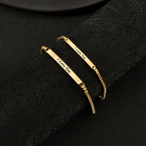 Close-up of gold couple bracelets with I Love You engraving on a brushed black surface