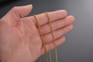 Primer plano detallado de la cadena de eslabones de oro de 18k entre dedos para grosor
