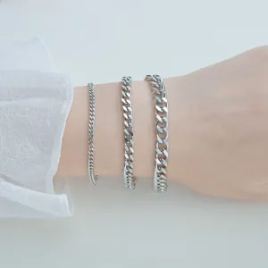 Close-up of three different widths of polished silver Cuban link chains on a wrist