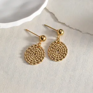 Macro detail of 14K gold minimalist flower earrings with woven texture on cream paper