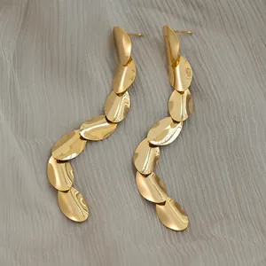 Minimalist oval tassel earrings in polished gold finish displayed on grey textured fabric