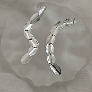 Macro detail of silver oval tassel earrings with polished metallic fringe on white fabric