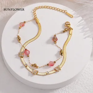 Double-layered golden bracelet with pink beads and zircon butterfly charms on white stand