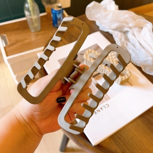 Dettaglio di una grande molletta per capelli kaki opaca tenuta in mano su un tavolo di legno