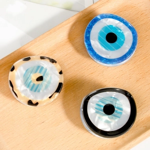 Drei Evil Eye Haarklammern in Blau, Bernstein und Schwarz auf einem Holztablett