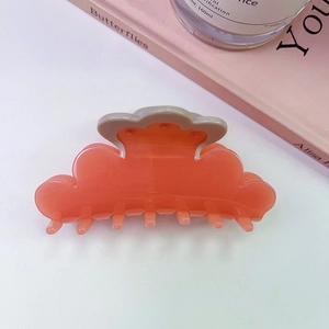 Macro detail of a shell-shaped coral pink hair claw clip with cream trim and glossy finish