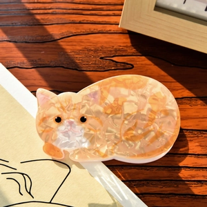 Detail of cute orange cat hair claw clip with marble texture on dark wood background