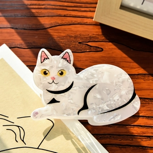 Detail of cute cat-shaped hair claw clip in white marble acetate on a wooden surface