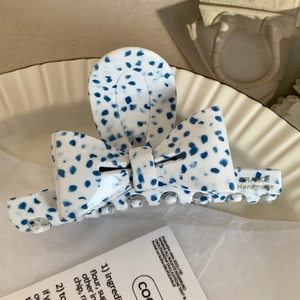 Détail d'une pince à cheveux nœud en acétate blanc à pois bleus et logo France Handmade