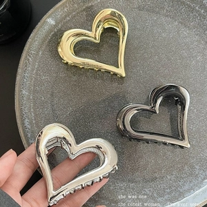 Hohle Herz-Haarklammern aus Metall in Gold, Silber und Schwarz auf grauem Tablett