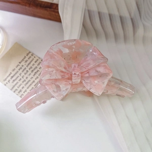Gros plan sur la pince à cheveux artisanale en acétate marbré rose avec nœud élégant
