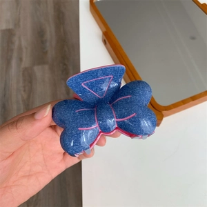 Pince à cheveux noeud en denim bleu avec doublure rose tenue dans la main
