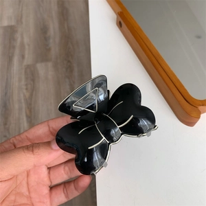 Vue détaillée d'une pince à cheveux noire avec nœud et bordure blanche à la main