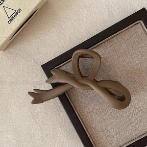 Detail of a matte dark coffee bow hair claw clip displayed on a rustic wooden stand
