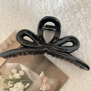 Close-up of a large glossy black bow hair claw clip on soft white plush background