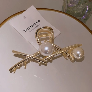 Close-up of golden metal hair claw with large white pearls on a minimalist ceramic plate