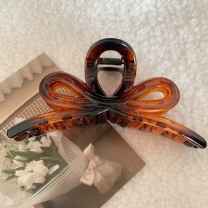 Detail of amber tortoiseshell bow hair claw clip on white fleece background texture