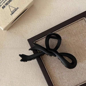 Detail view of a large black matte bow hair claw clip on a textured linen background