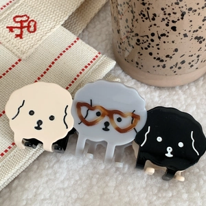 Detalle de tres pequeñas pinzas para el cabello con forma de perro en crema, gris y negro