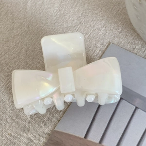 Close-up of small acetate bow hair claw clip with pearlescent ivory finish and sturdy teeth