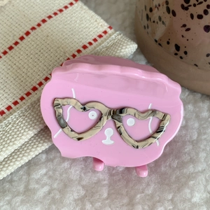 Detalle de pinza para el pelo rosa con forma de nube y gafas de corazón en acabado carey