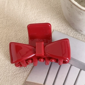 Detailed view of a bright red bow-shaped hair claw clip on a beige linen background