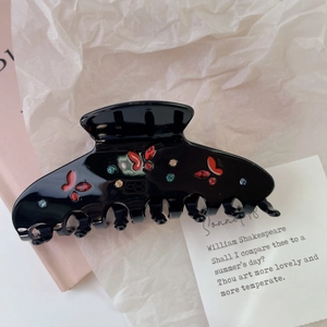 Detailed shot of black acetate hair claw clip with red crystal butterflies on white paper