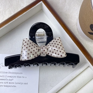Primo piano di una pinza per capelli in acetato nero con fiocco a pois beige su un vassoio