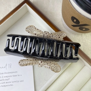 Dettaglio di un fermaglio per capelli nero lucido con fiocchi beige a pois in una scatola regalo