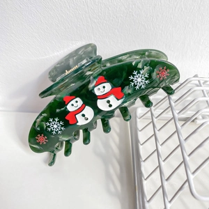 Gros plan sur la pince à cheveux en acétate vert marbré avec motifs de bonhomme de neige