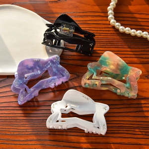 Detailed view of four acetate hair clips with marble patterns and rhinestones on wood
