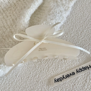 Close-up of cream acetate hair claw with delicate ribbon bow and gold lettering detail