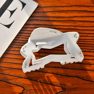 Detail view of a white cutout star hair claw clip with rhinestones on a wooden surface