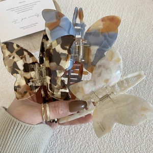 Close-up of butterfly-shaped acetate hair claws with marble texture and gold lettering