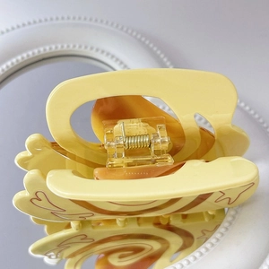 Detailed close-up of pale yellow heart hair claw with brown swirls on a mirror surface