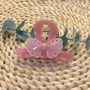 Pince à cheveux noeud rose en acétate avec détails de coeurs évidés sur fond de paille