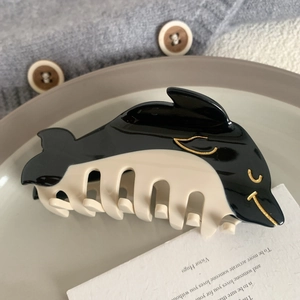 Detail view of a glossy black and beige whale-shaped hair claw clip on a porcelain plate