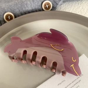 Detail of dolphin hair claw clip in purple gradient resin with gold accents on grey knit