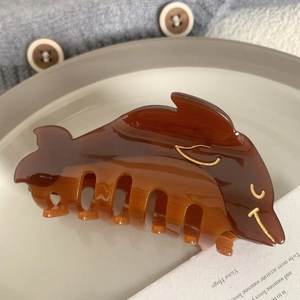 Detailed view of a brown dolphin-shaped acetate hair claw clip on a ceramic tray
