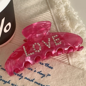 Pink resin hair claw clip with crystal LOVE lettering on beige fabric backdrop