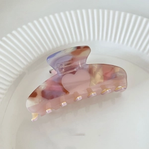 Detail of pink marble acetate hair claw with heart patterns on a striped ceramic plate