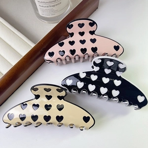 Three acetate hair claws with heart patterns in pink, black, and beige colors