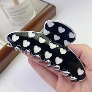 Close-up of a large black acetate hair claw clip featuring white heart pattern details